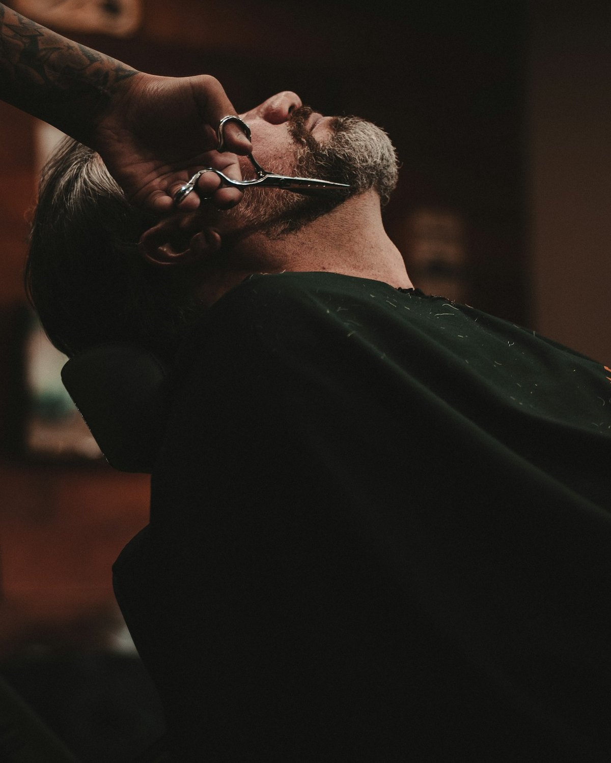 A barber working on a reclined customer, the shop dark behind them